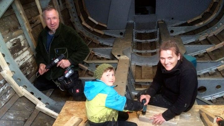 Drei Männer und ein Kind arbeiten an einem Holzboot.